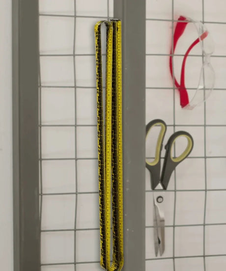 Yellow measuring tape, scissors, and red safety glasses on a wire grid organizer.