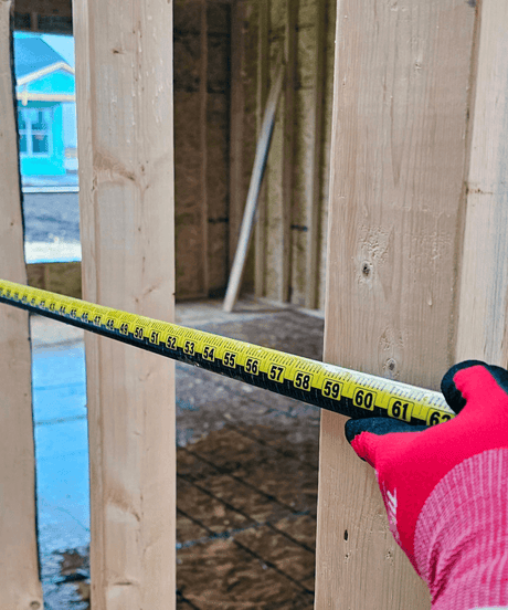 Hand in red glove measuring wooden frame with yellow tape measure during home construction