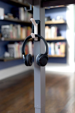 Black headphones hanging from a Victor® Technology MagnaTrack mount on a gray desk leg.