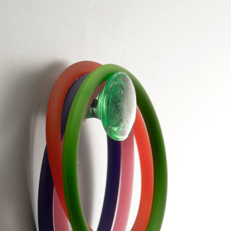 Colorful rubber bands on a green suction hook attached to a white wall