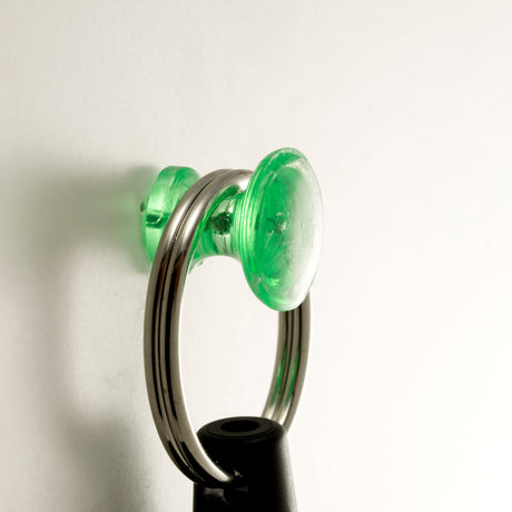 Green magnetic push pin holding key ring on white wall