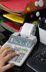 Calculator with printing paper on office desk near folders, pens, and a keyboard