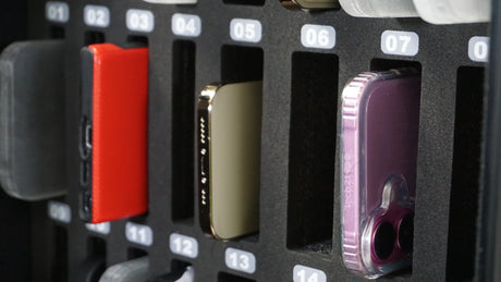 Row of smartphones in numbered foam organizer slots, including red and purple cases