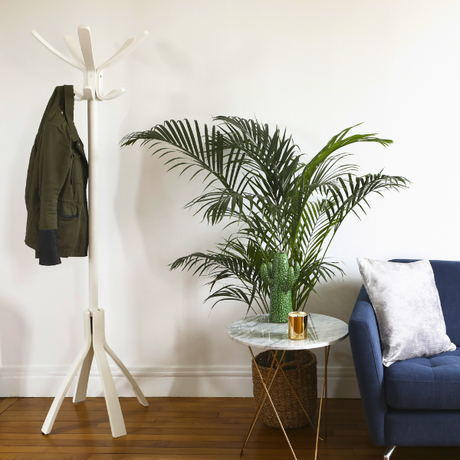 White wood coat stand with jacket beside plant, marble side table, and blue sofa in modern room