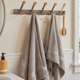 A gray wall-mounted towel rack with six hooks, shown in a bathroom setting with two gray towels hanging on it and a wooden brush on one hook.