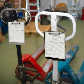 Two Officemate magnetic clipboards attached to industrial pallet jack handles in a warehouse.