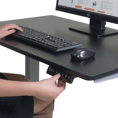Person using a height-adjustable desk with a computer setup.
