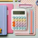 Pastel desktop calculator with large buttons on a desk with notebooks, clipboard, pencils.