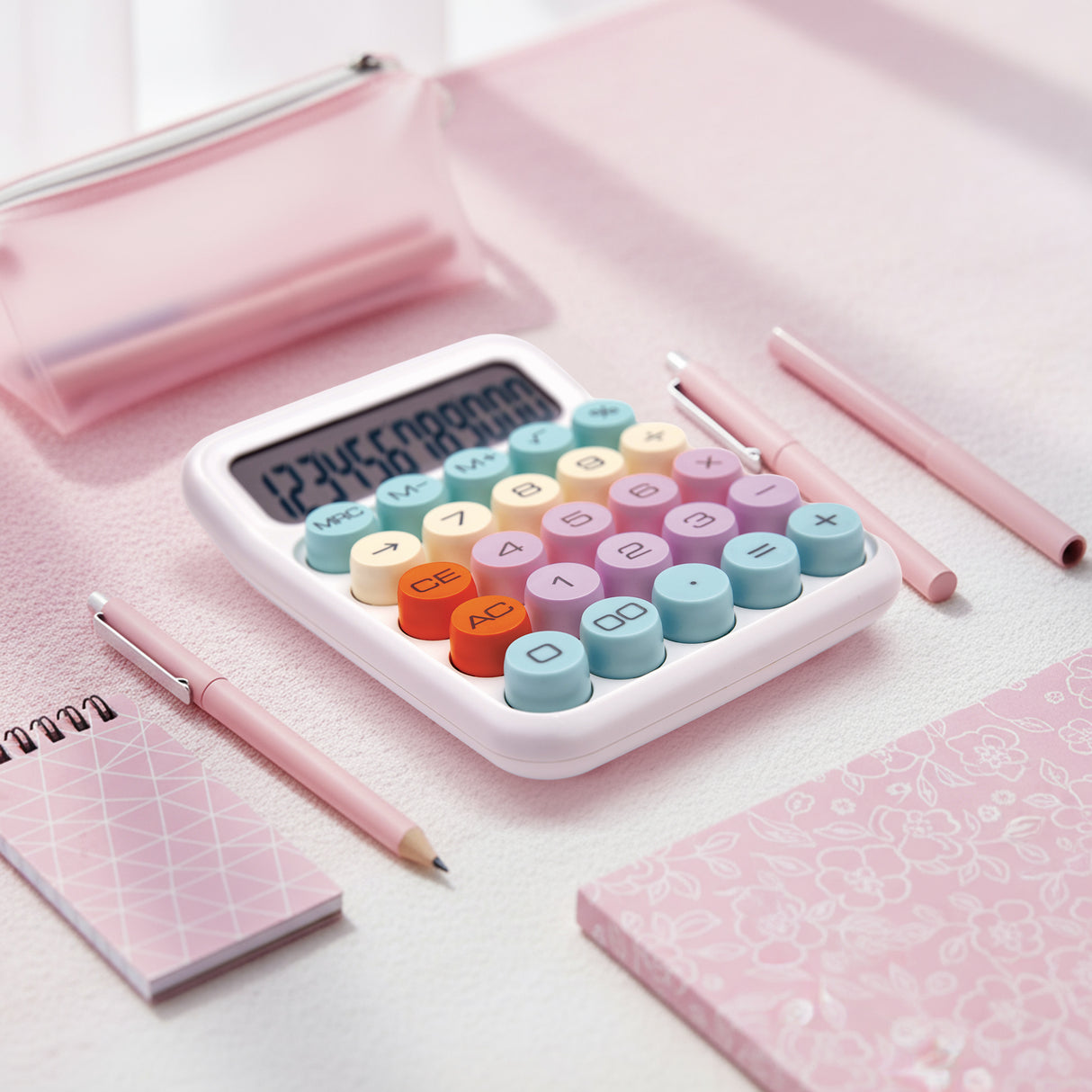 Colorful desktop calculator with round buttons on a pink workspace, surrounded by stationery.