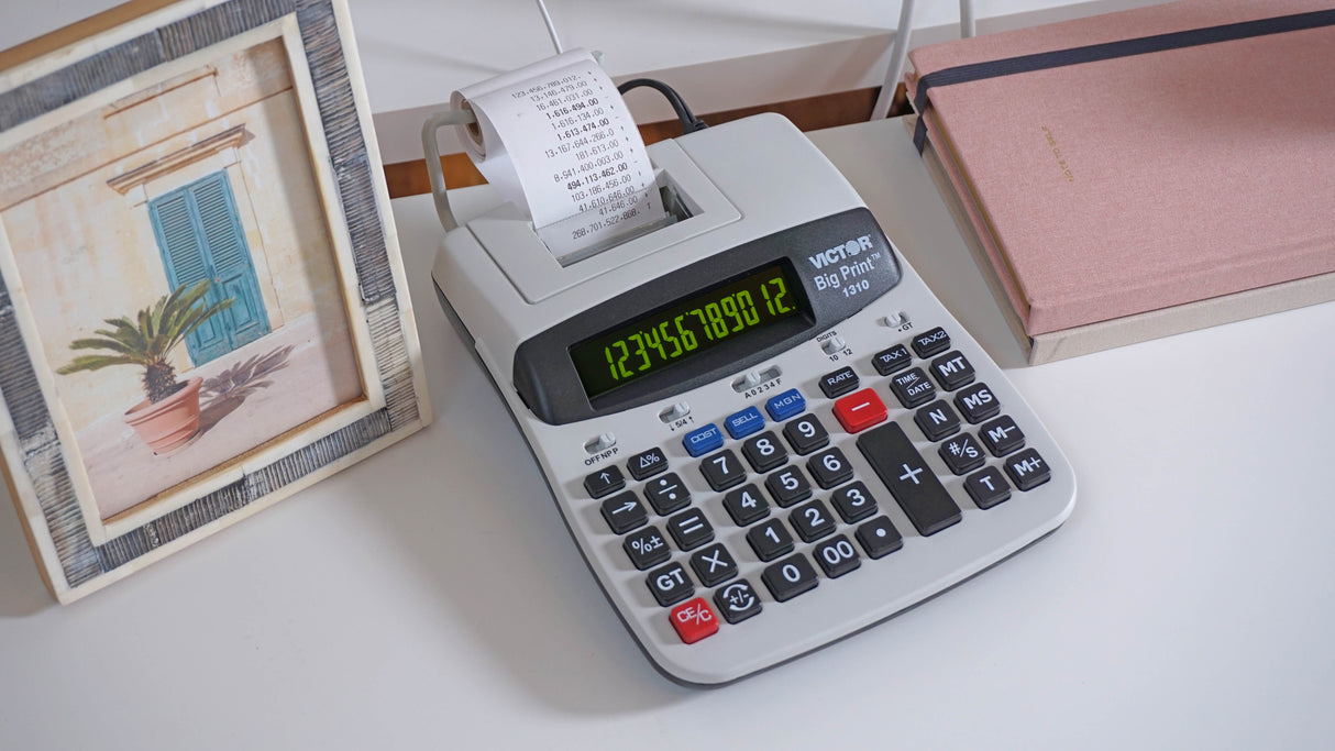 Desktop thermal printing calculator with large display and paper roll, next to notebooks and a photo frame