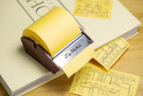 Yellow Zip Notes dispenser with attached notes on a wooden surface